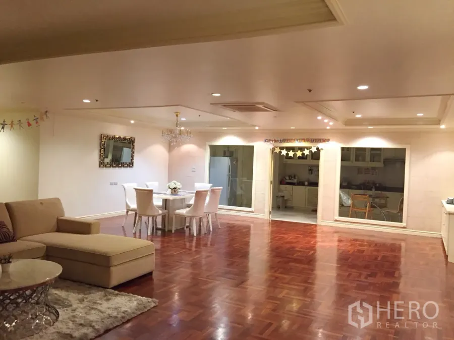 Condominium for rent in Watthana, Bangkok - Spacious open-plan living and dining area with parquet wood floors, recessed lighting, a chandelier, and interior windows looking into the kitchen.