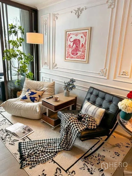 คอนโด ให้เช่า - มุมพักผ่อนพร้อมเก้าอี้เอน ผนังบัวปูนปั้น โคมไฟยืน และต้นไม้ริมหน้าต่างสูง