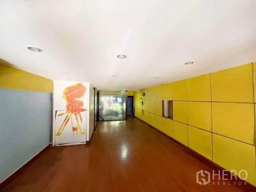 Shophouse for rent in Bang Rak, Bangkok - Elongated workspace with yellow paneled wall, recessed lights, wood floor, and glass entry.