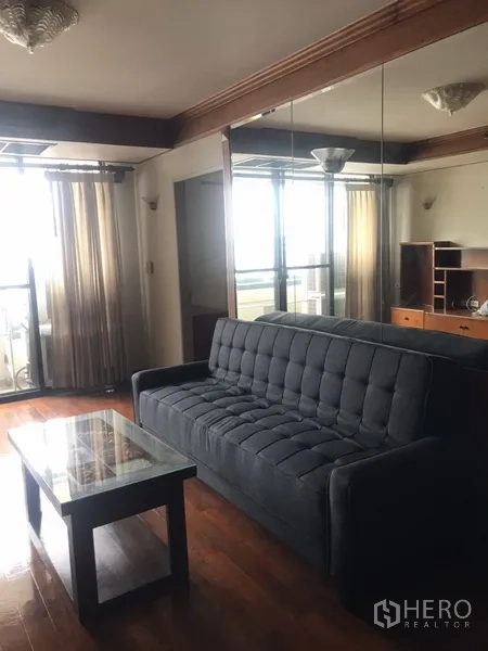 公寓 出租在Watthana, Bangkok - 客厅配灰色沙发、阳台落地门与镜面墙，木地板。