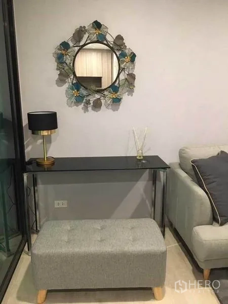 คอนโด ขายในBang Na, Bangkok - มุมคอนโซลกะทัดรัด โต๊ะกระจก กระจกติดผนังทรงกลม พัฟ และโคมไฟโมเดิร์นข้างโซฟา