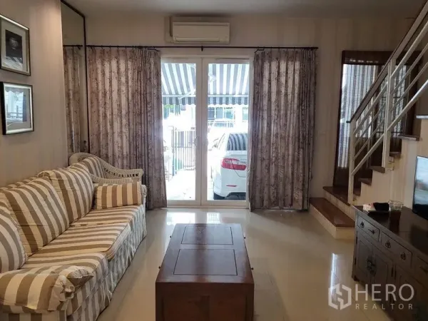 Townhouse for rent in Wang Thonglang, Bangkok - Living room with striped sofa, coffee table and glass doors opening to a carport.