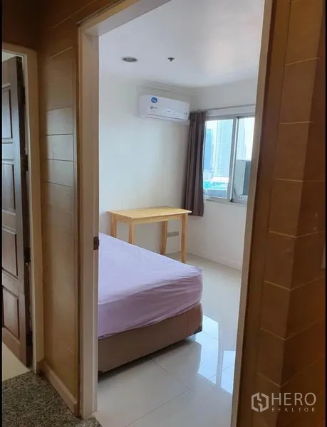Condominium for rent in Ratchathewi, Bangkok - Doorway view into airy bedroom with air conditioner and city-facing window.