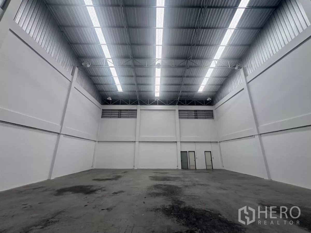 Factory for rent in Phra Samut Chedi, Samut Prakan - Back wall of the warehouse with service doors beneath bright roof lights.
