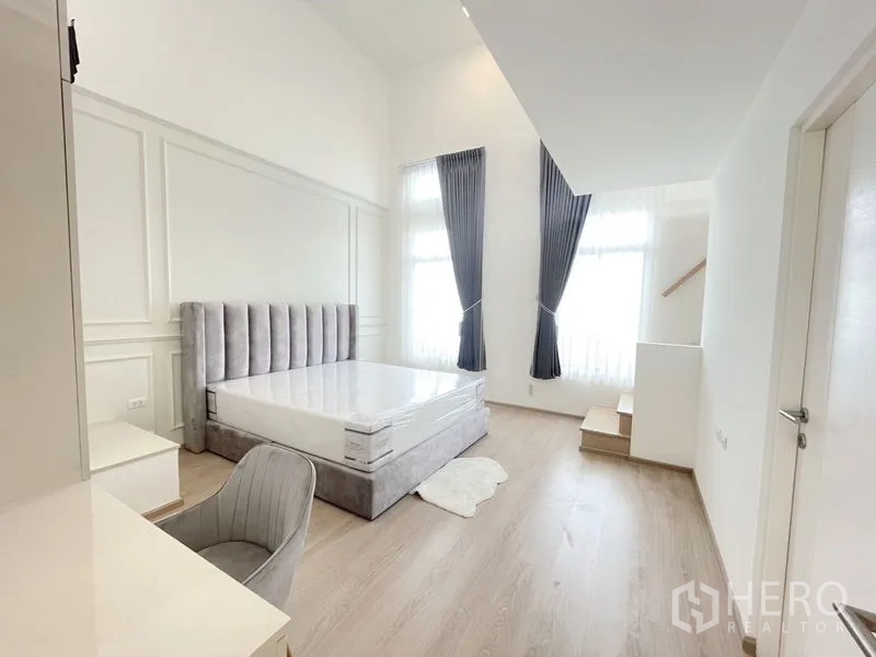 联排别墅 出租在Prawet, Bangkok - 主卧挑高空间，落地窗与通往夹层的小阶梯。