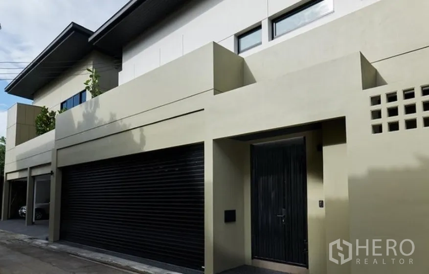 บ้าน ให้เช่าในWatthana, Bangkok - ด้านหน้าบ้านเดี่ยวสไตล์โมเดิร์น ประตูโรงรถสีดำและประตูไม้ทึบ