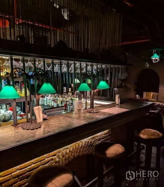 零售空间 出租 - 带绿色灯罩的长吧台，镜面后吧与吧凳，工业风格场景。