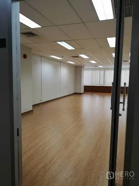 办公空间 出租在Watthana, Bangkok - 入口视角的空置办公室，木纹地板、格栅吊顶、日光灯和百叶窗。