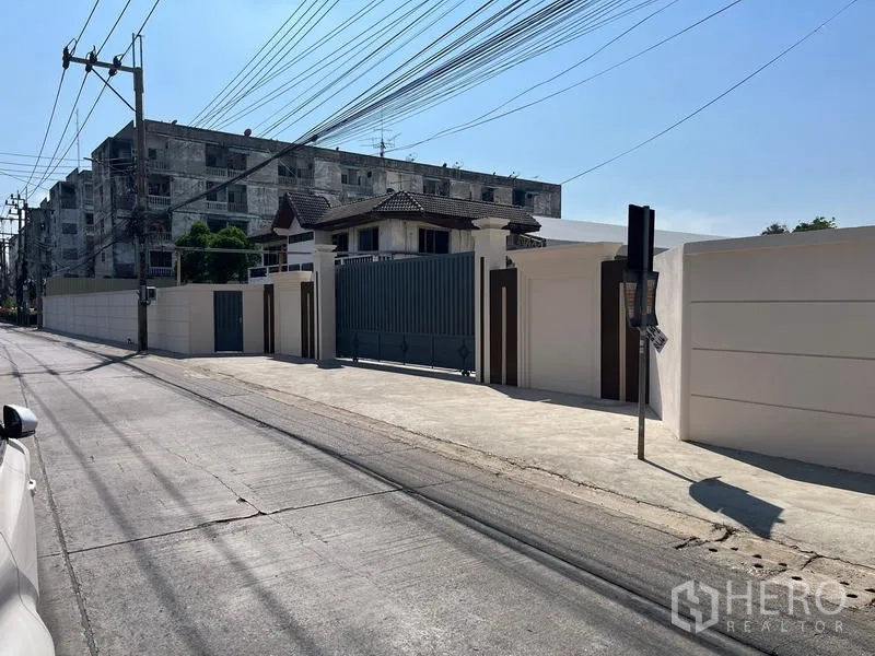Warehouse for rent or sale - Gated industrial entrance with high perimeter walls along a quiet road in Nong Khaem, Bangkok.