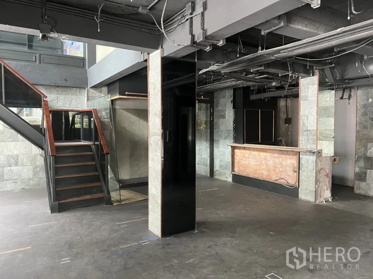 零售空间 出租在Khlong Toei, Bangkok - 一层零售区，楼梯、服务吧台、外露顶棚与石材饰面。