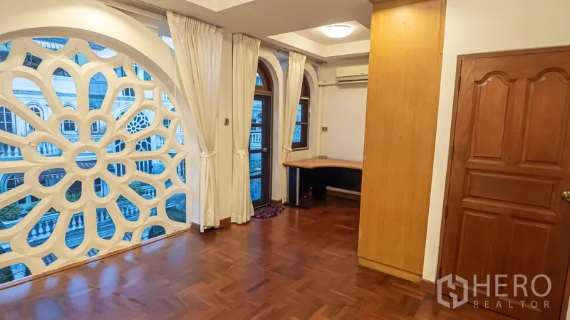 Townhouse for rent in Khlong Toei, Bangkok - Bedroom with parquet flooring, arched windows and geometric screen plus built‑in desk.