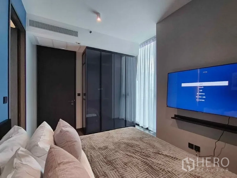 Condominium for rent in Bang Rak, Bangkok - Bedroom view showing wardrobe, natural light through sheer curtains, and TV.