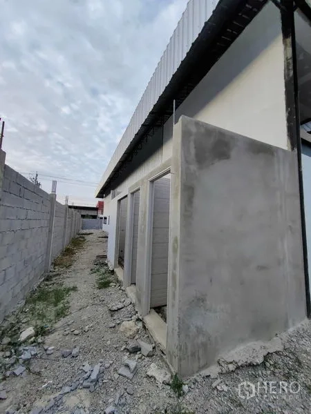 Factory for rent or sale in Mueang Samut Prakan, Samut Prakan - Side alley showing exterior restroom doors beneath a metal awning.