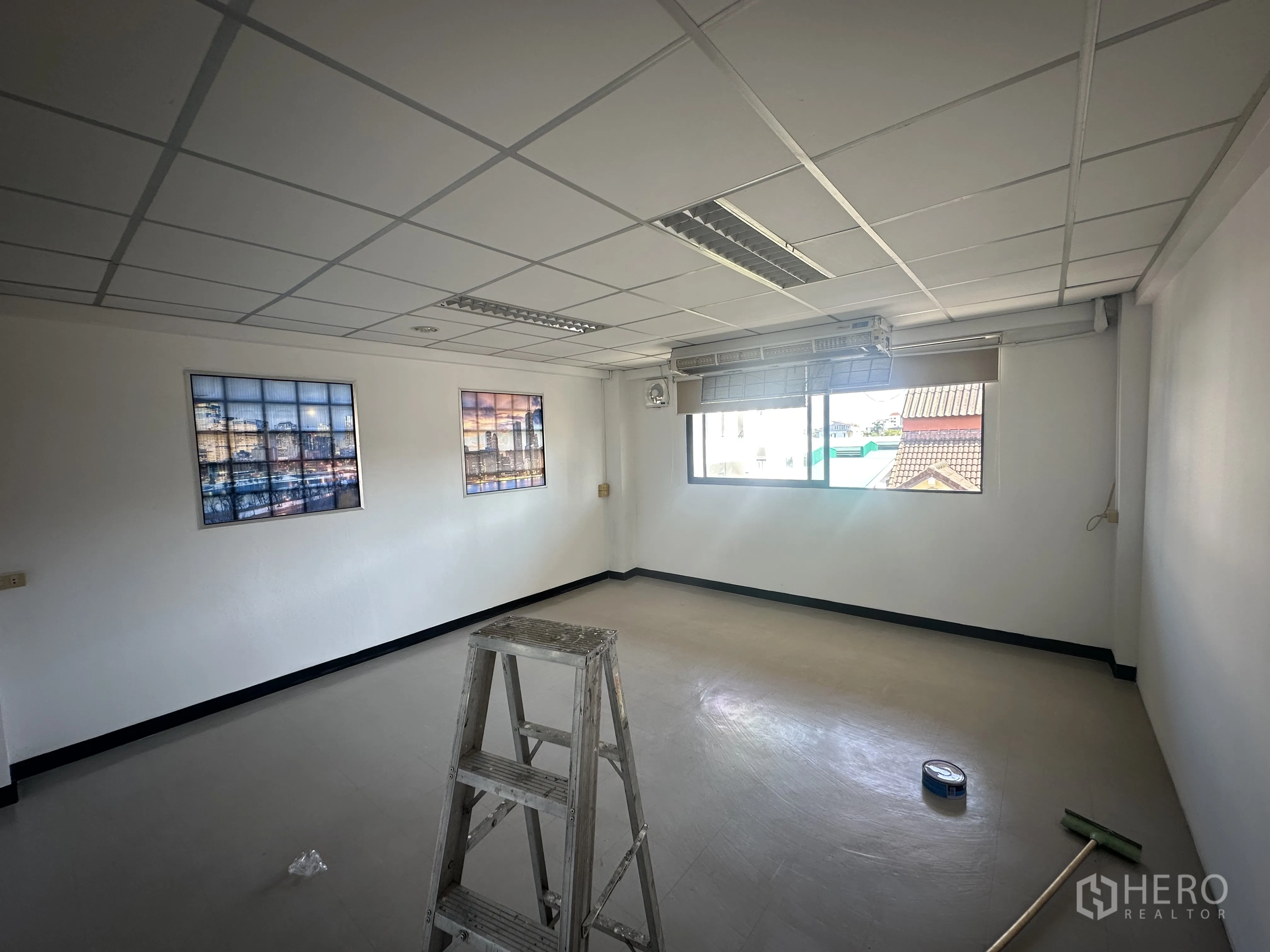 Office Space for rent in Watthana, Bangkok - Secondary office room with window and roller blind, framed artwork, ladder and cleaning tools on the floor.