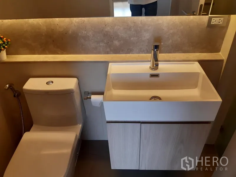 Condominium for rent in Khlong Toei, Bangkok - Contemporary bathroom with vanity sink, long mirror shelf and toilet.