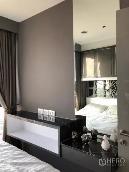 Condominium for rent in Khlong Toei, Bangkok - Bedroom corner with black marble vanity, mirror and overhead cabinets.