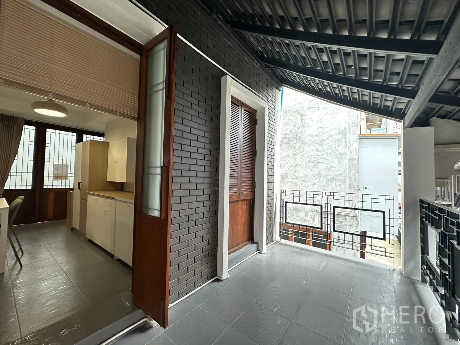 Apartment for rent in Pathum Wan, Bangkok - Semi-open terrace leading to a kitchen area with brick wall and wooden doors.