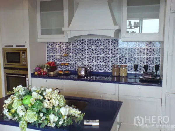Condominium for rent in Khlong Toei, Bangkok - Modern white kitchen with island, built-in oven and blue-and-white backsplash.
