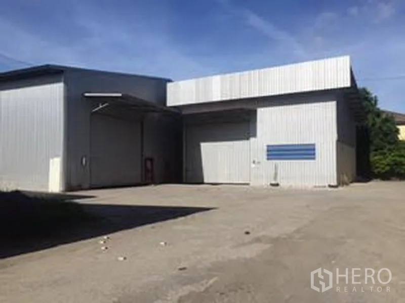 Warehouse for rent in Sai Mai, Bangkok - Two adjoining steel warehouses with roller doors and an expansive paved yard for truck access.