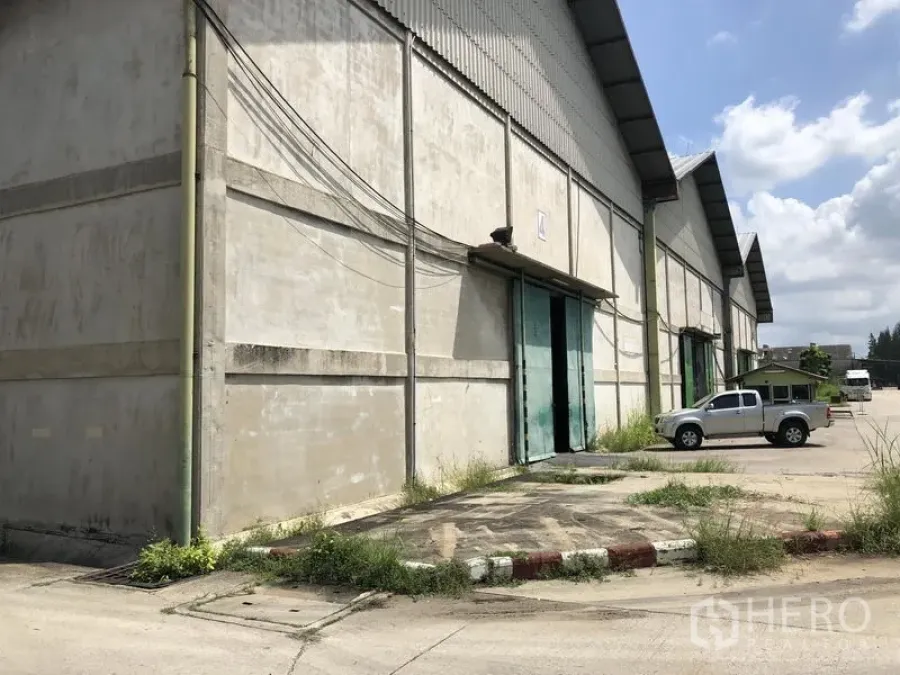 货栈 出租在Mueang Pathum Thani, Pathum Thani - 巴吞他尼市区大型仓库外观，绿色推拉门，装卸硬化场地与停车区。