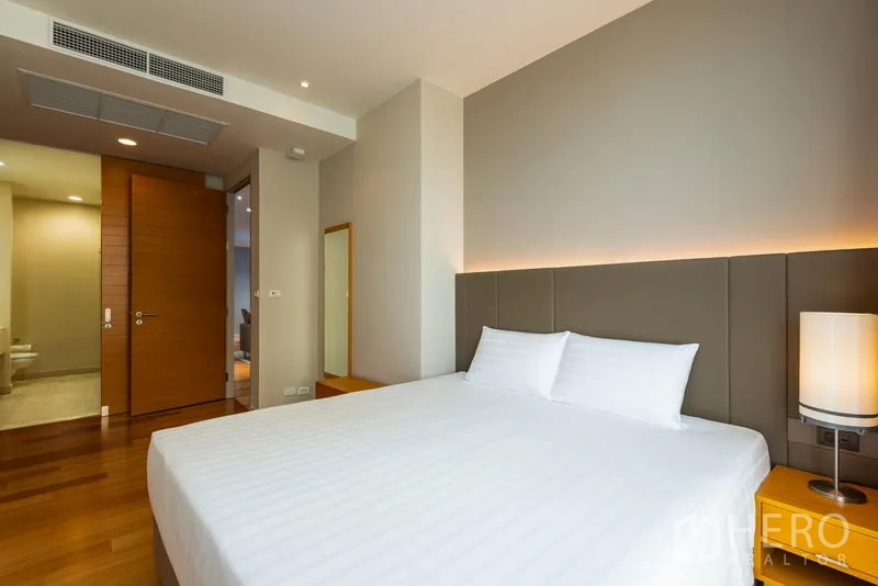 คอนโด ให้เช่าในBang Kho Laem, Bangkok - ห้องนอนหลักเตียงคิงพร้อมไฟซ่อนหัวเตียง พื้นไม้ และมุมมองไปยังห้องน้ำในตัว