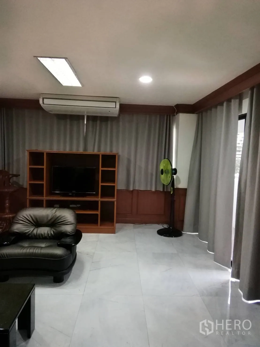 คอนโด ให้เช่าหรือขายในWatthana, Bangkok - มุมห้องนั่งเล่นมีชั้นวางทีวี แอร์แบบแยกส่วน และผ้าม่านทึบสีเทา