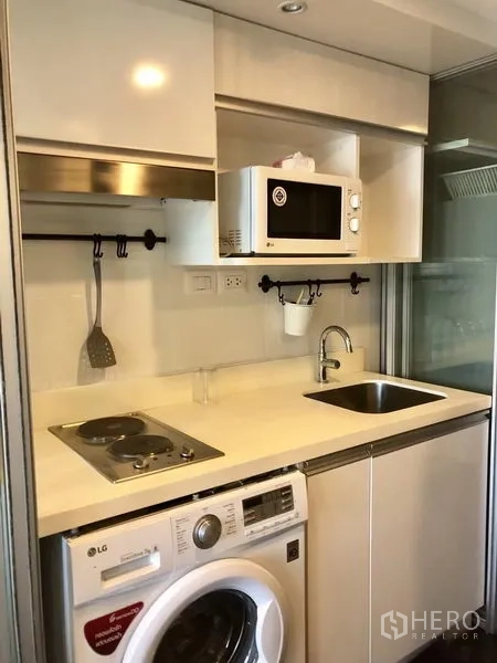 公寓 出租在Khlong Toei, Bangkok - 白色紧凑型厨房，配电磁炉、水槽、微波炉与洗衣机。