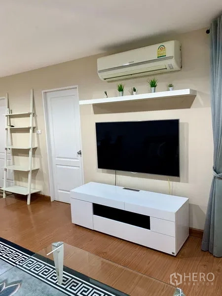 Condominium for rent in Huai Khwang, Bangkok - TV feature wall with floating shelf, white media cabinet and split-type air conditioner.
