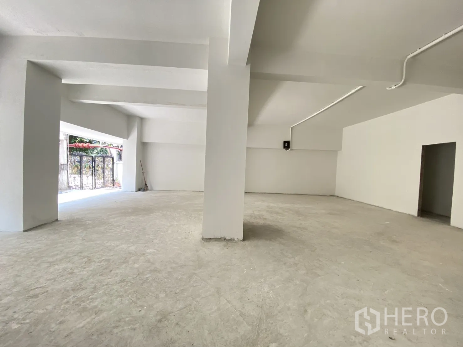 零售空间 for rent in Watthana, Bangkok - 店内纵深朝向栅栏式入口，白墙与管线清晰可见。