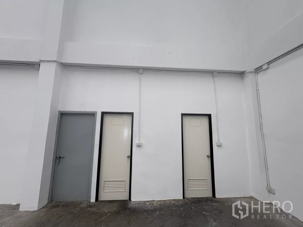 Factory for rent in Phra Samut Chedi, Samut Prakan - Close-up of internal service doors and exposed electrical conduits on a white wall.