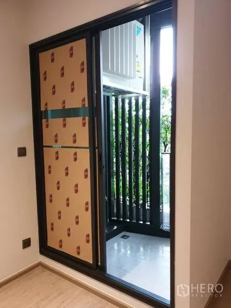 Condominium for sale in Watthana, Bangkok - Sliding glass door from the living area to a small balcony with air-con unit and louvered screen.