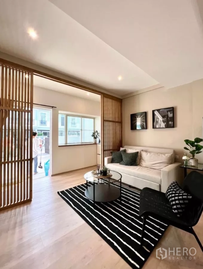 联排别墅 出租在Prawet, Bangkok - 客厅通向前庭，木格栅屏风与黑白条纹地毯相映成趣。