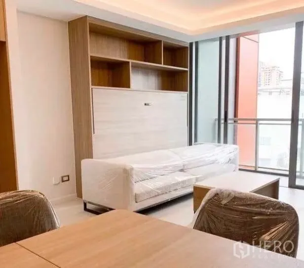 Condominium for sale in Ratchathewi, Bangkok - Living room with balcony access, built‑in shelving and dining chairs in the foreground.