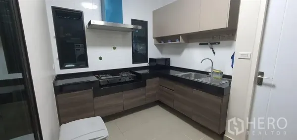 Detached House for rent in Bang Phli, Samut Prakan - Modern L-shaped kitchen with gas hob, hood, black countertops and ample cabinetry