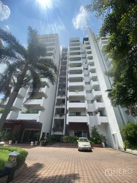 Condominium for rent - High-rise condominium exterior with white facade, balconies, driveway and palm tree on a sunny day.