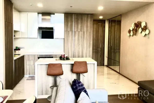 Condominium for rent in Watthana, Bangkok - Bright modern kitchen with wood cabinetry, white countertops, and an island with two bar stools.