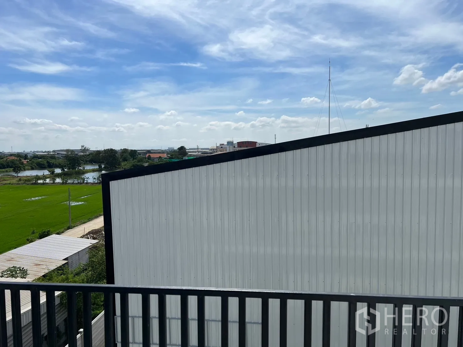 货栈 出租在Bang Sao Thong, Samut Prakan - 阳台视角下，屋顶、绿田与水域景观，蓝天白云。