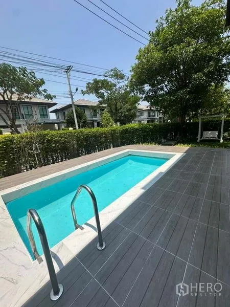 Detached House for sale in Prawet, Bangkok - Pool view from deck with hedges, trees and neighboring homes in a gated estate.