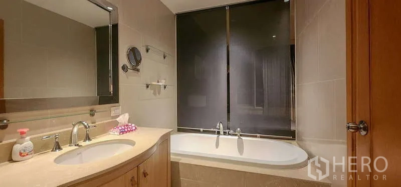 Condominium for sale in Sathon, Bangkok - Bathroom featuring built-in vanity and soaking bathtub with window and roller shade.