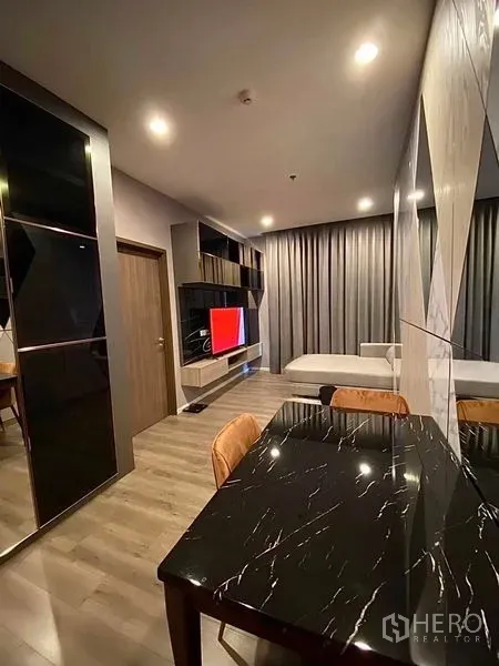 Condominium for rent in Phra Khanong, Bangkok - Open-plan living area with a black marble dining table, custom TV wall, sofa and full-height curtains.