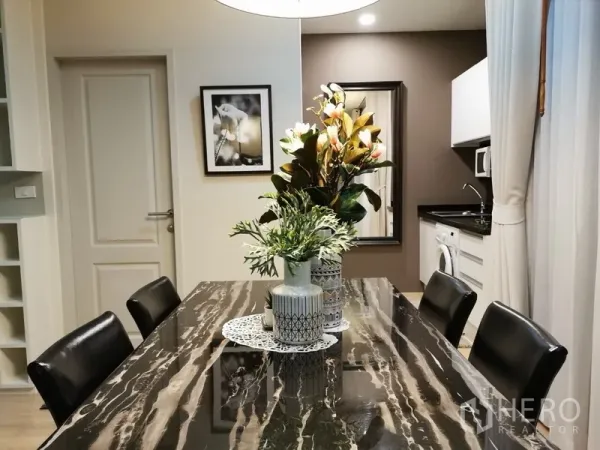 公寓 出售在Bangkok - 现代餐区，黑色大理石餐桌与花艺装饰，旁连带洗衣机与微波炉的精巧厨房。