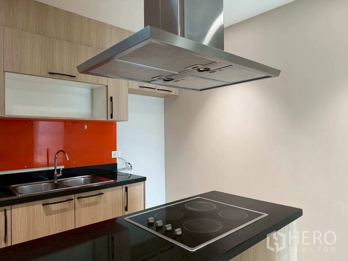 Condominium for rent or sale in Khlong Toei, Bangkok - Close-up of kitchen island with electric hob and stainless range hood.