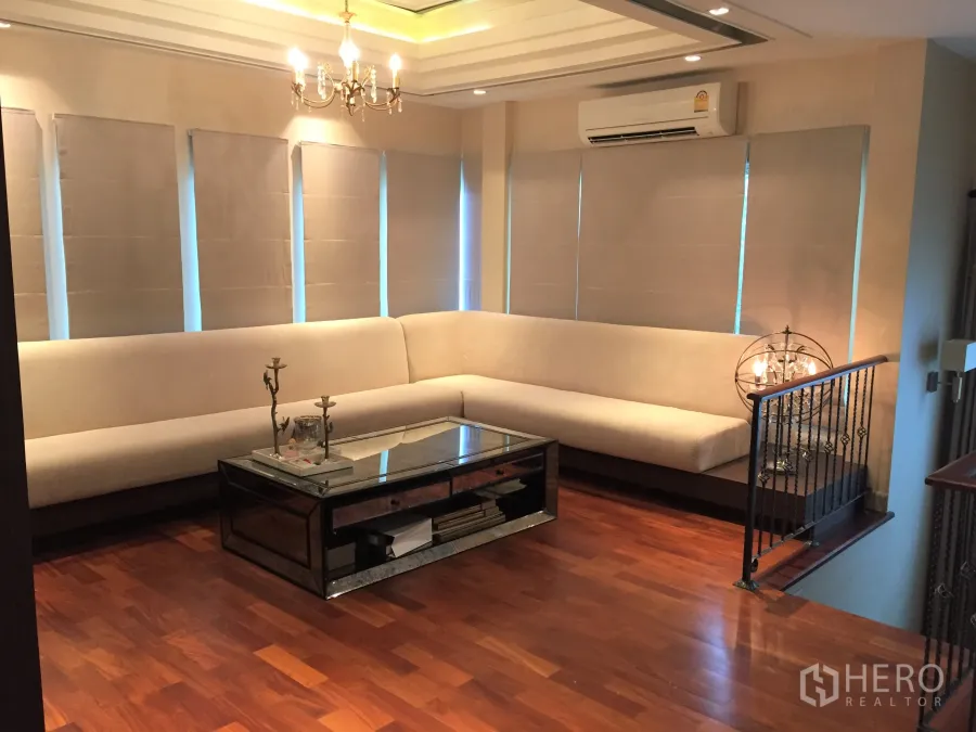 Detached House for sale in Saphan Sung, Bangkok - Elegant living room with L-shaped beige sofa, chandelier ceiling and polished wood floors.