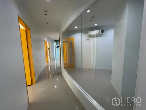 Office Space for rent in Khlong Toei, Bangkok - Long hallway with glossy tiles, a glass wall and bright yellow doors leading to private rooms.