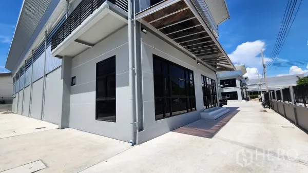 Factory for rent or sale in Bang Bo, Samut Prakan - Corner office facade with tinted windows, canopy and spacious driveway within a new industrial compound.