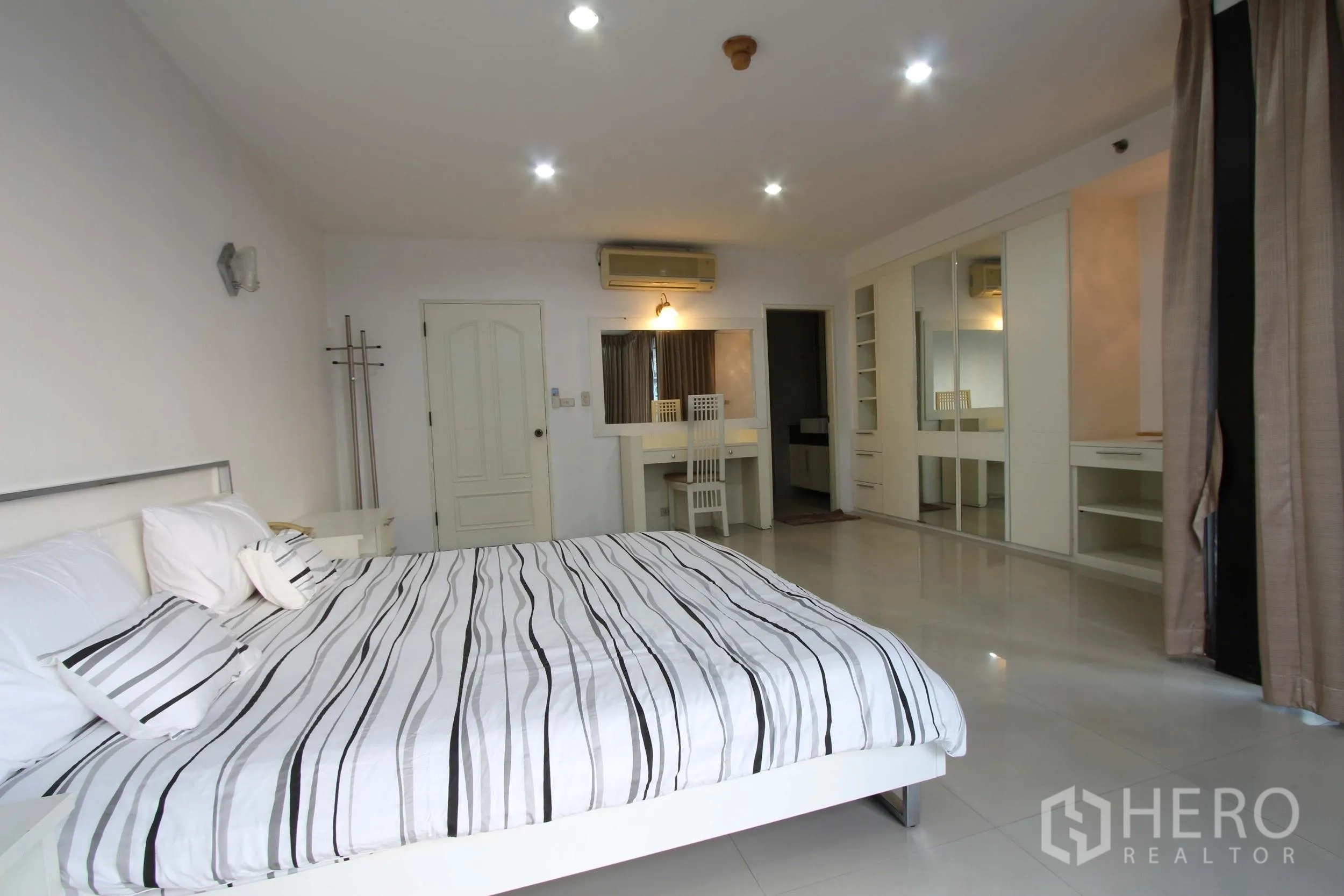 Condominium for rent in Watthana, Bangkok - Spacious master bedroom with striped bedding, wall-to-wall wardrobes, vanity desk, and recessed lighting.