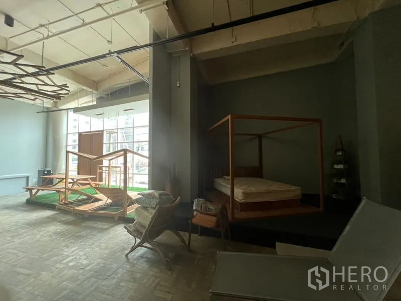 零售空间 出租在Khlong Toei, Bangkok - 展示区挑高、落地窗充足采光，抬高平台上陈列一张床。