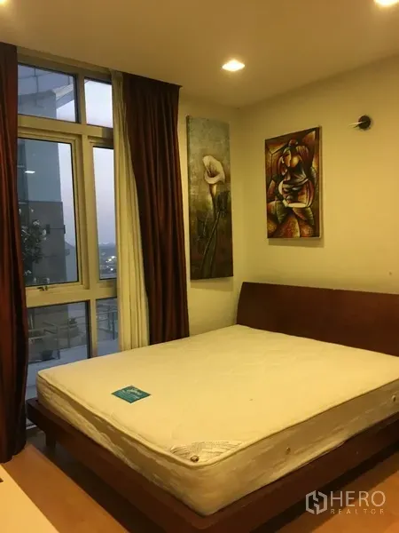 Condominium for rent in Khlong Toei, Bangkok - Bright bedroom with large windows, brown curtains, and city-facing balcony.
