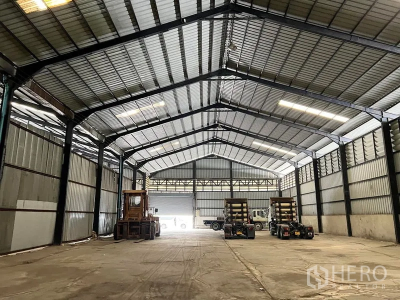 Warehouse for rent in Phra Samut Chedi, Samut Prakan - Warehouse interior showing loading area with tall roof and vehicles.
