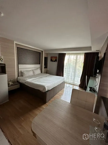 Apartment for rent in Khlong Toei, Bangkok - Furnished studio bedroom with bed, TV and sliding doors to a balcony.